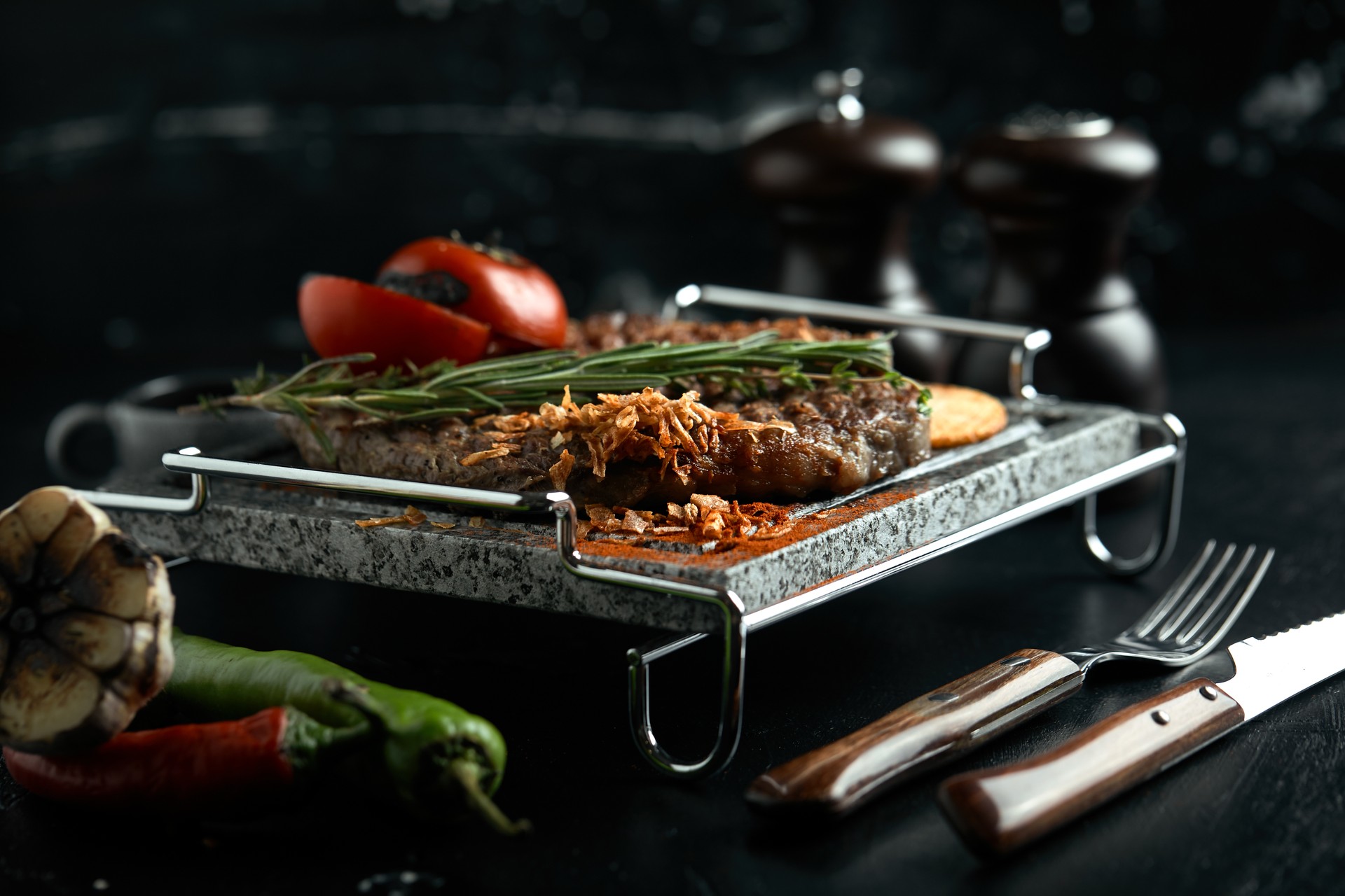 Grilled steak with knife and fork carved on black stone slate. Steak on a hot marble stone. Copy space, dark background, food fashion photo.